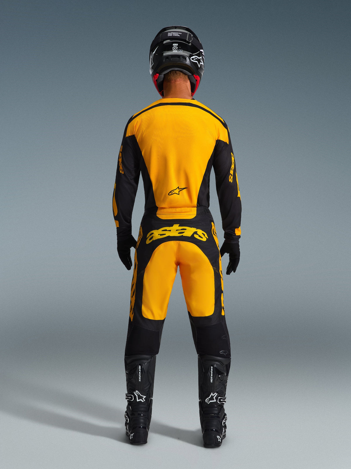 Motocross rider from the back wearing the Alpinestars 2026 Racer Riway Gear Set, Yellow and Black jersey and pants, features 'astars' branding on the rear, paired with black helmet, gloves, and boots, complete off-road racing kit