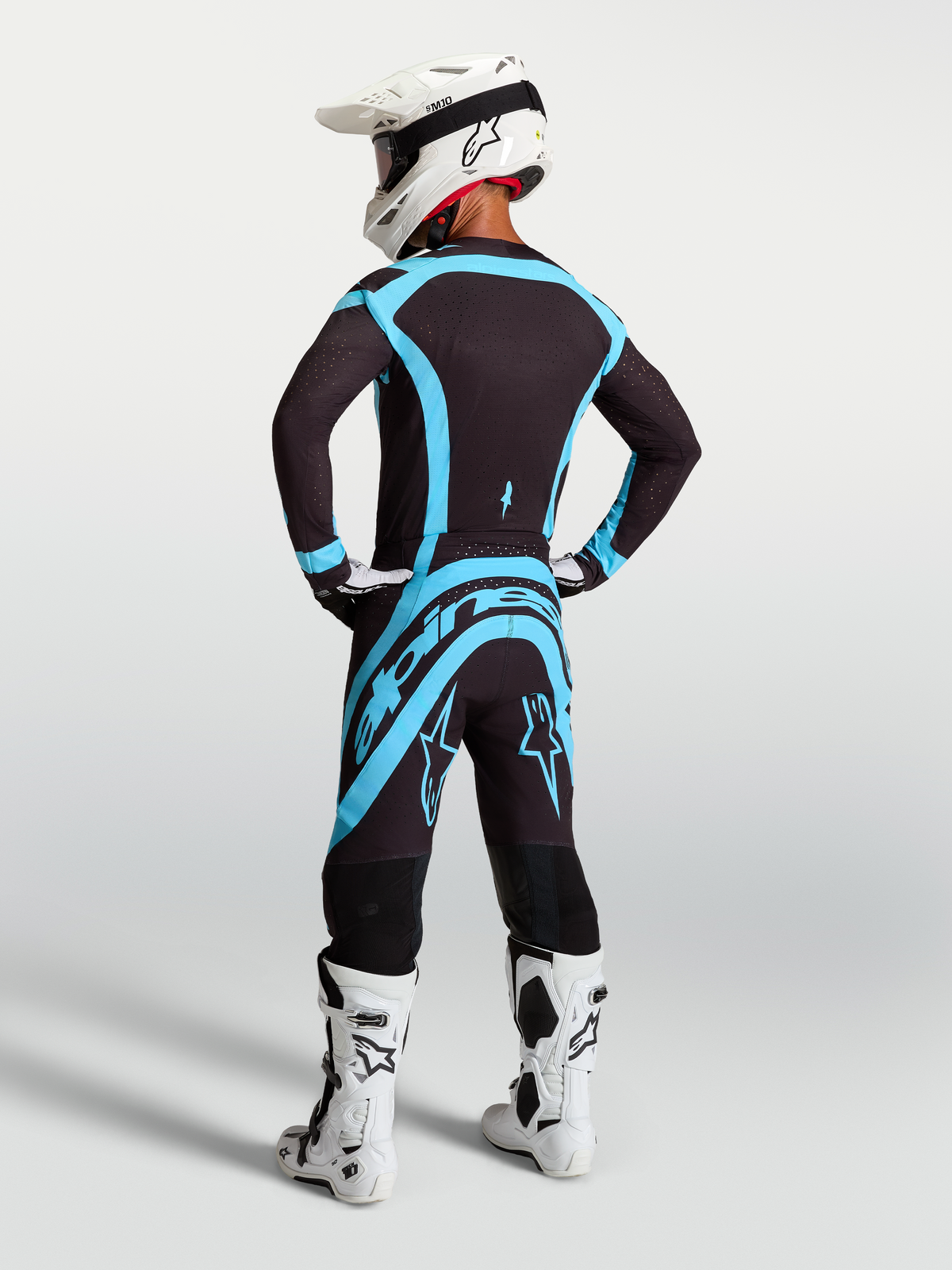 Alpinestars 2027 Supertech Vesta Jersey and Gear Set, black and turquoise motocross outfit with white boots, rear view.