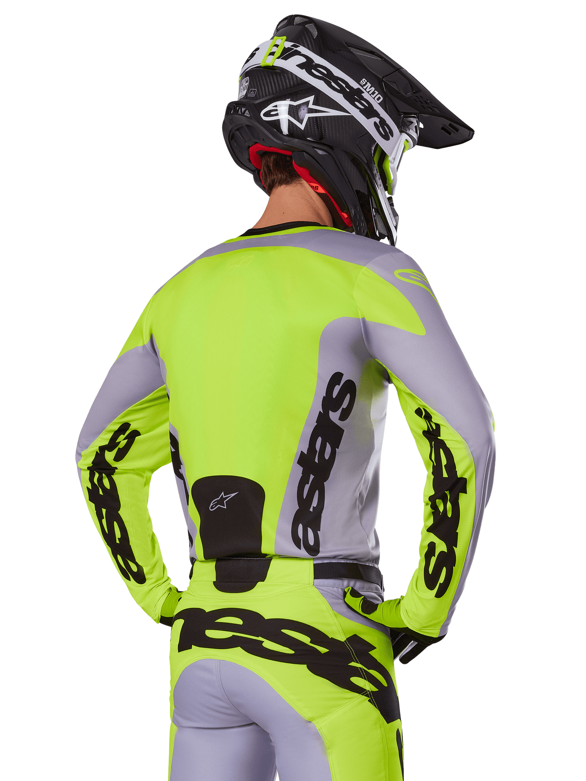 Piloto de motocross visto de trás com a camisola Alpinestars 2025 Racer Veil em cinzento e amarelo néon, com a marca 'astars' em destaque nas costas e mangas, calças a condizer e capacete preto para um visual de competição completo.