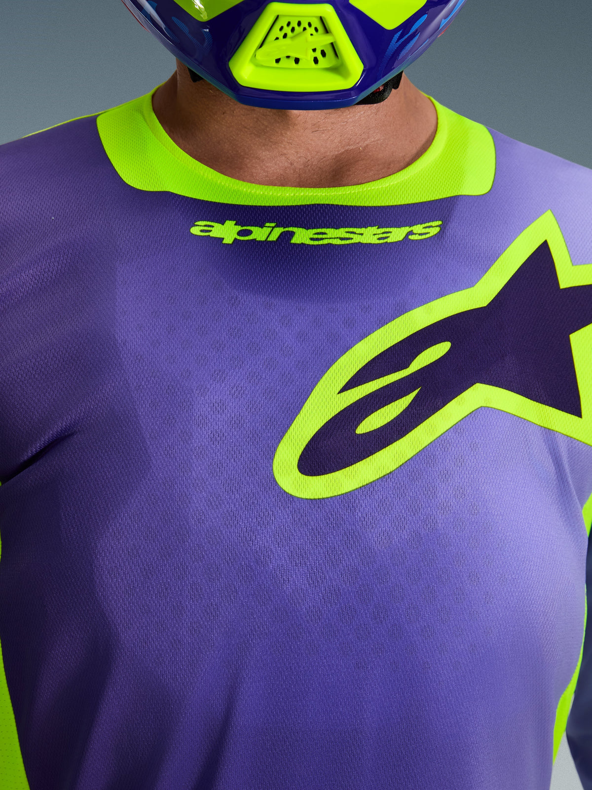 Alpinestars 2026 Racer Portl Jersey, Purple and Yellow Fluo, close-up shot of the chest and collar area featuring the Alpinestars wordmark and star logo, worn with a matching motocross helmet, technical off-road racing apparel.
