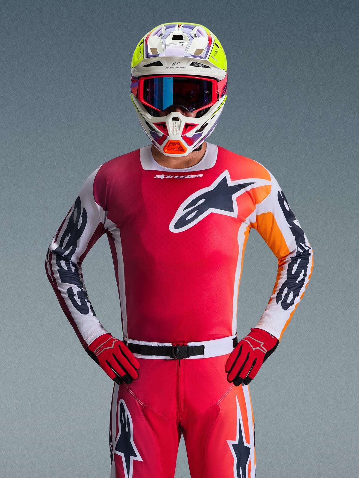 Alpinestars 2026 Racer Portl Gear Set, piloto de motocross a usar uma camisola vermelha vibrante com detalhes em laranja e branco, calças e luvas vermelhas a condizer, capacete multicolorido com realces em amarelo néon e óculos azuis, logótipo de estrela grande no peito, equipamento profissional de corrida todo-o-terreno