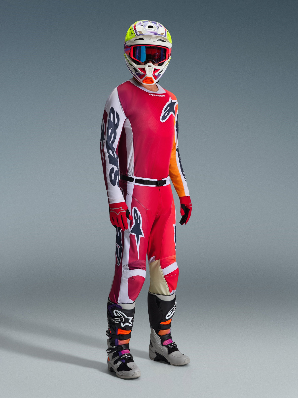 Piloto de motocross com o Conjunto de Equipamento Alpinestars 2026 Racer Portl, composto por uma camisola vermelha e branca com a marca 'Astars' em destaque na manga, calças vermelhas e brancas a condizer, um capacete branco e amarelo coordenado com óculos de armação vermelha e botas de motocross cinzentas e pretas, equipamento completo para corridas todo-o-terreno.