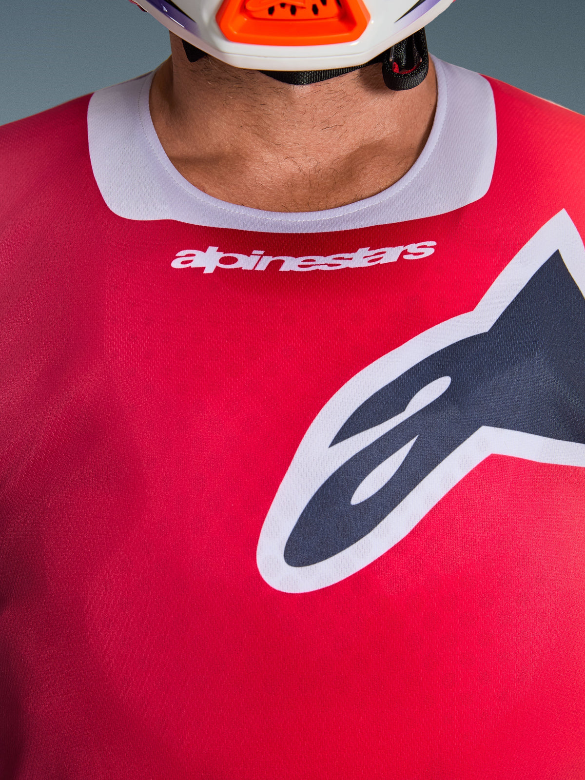 Camisola Alpinestars 2026 Racer Portl, vista em pormenor da zona do peito e da gola, vermelha com acabamento da gola em cinzento claro, texto Alpinestars a branco e logótipo Astars grande, apresentando uma textura de tecido técnico que absorve a humidade