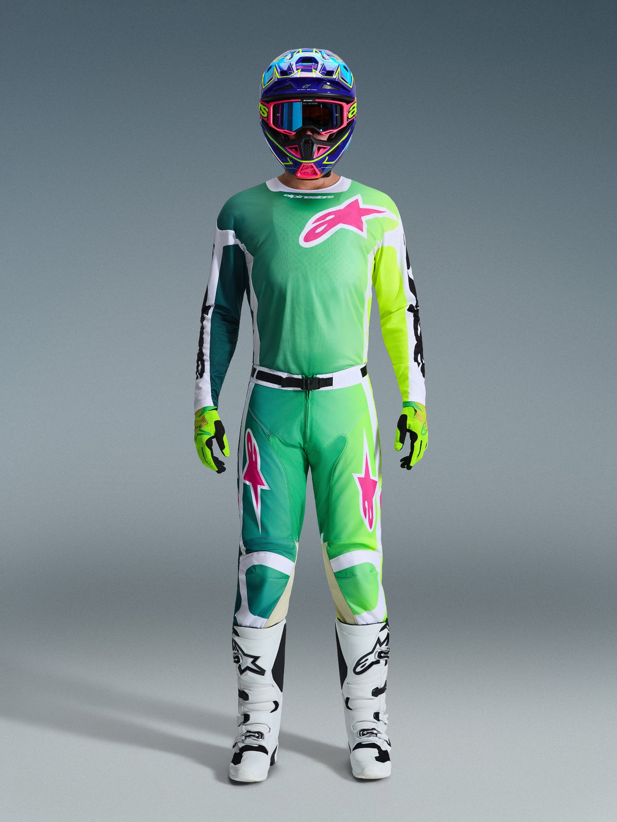 Conjunto de equipamento Alpinestars Racer Portl 2026, piloto de motocross com camisola em verde, branco e preto, com pormenores vibrantes em cor-de-rosa e verde-lima e um grande logótipo de estrela no peito, combinada com calças a condizer, capacete colorido, luvas verde-lima e botas de motocross brancas