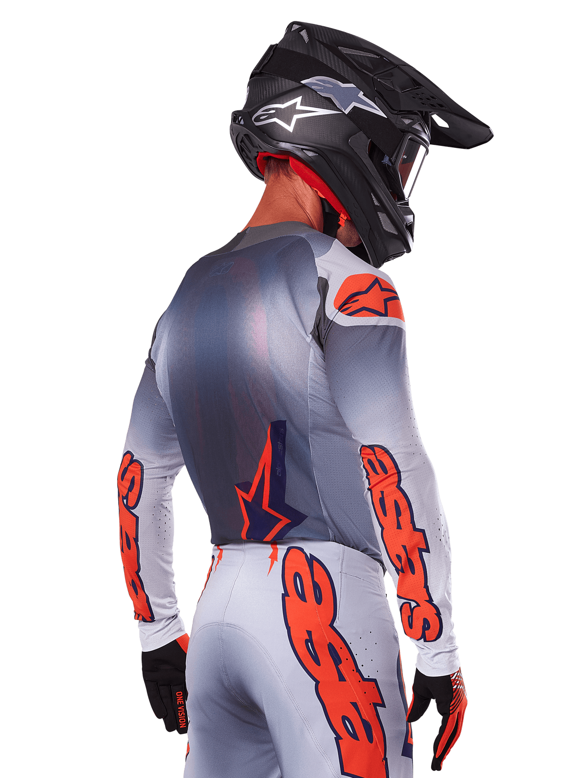 Piloto de motocross visto de costas a usar a camisola Alpinestars 2025 Supertech Lipan em cinzento e laranja fluorescente, com logótipos laranja de destaque nas mangas e costas, combinada com calças a condizer e capacete preto, equipamento de corrida profissional para performance em todo-o-terreno.
