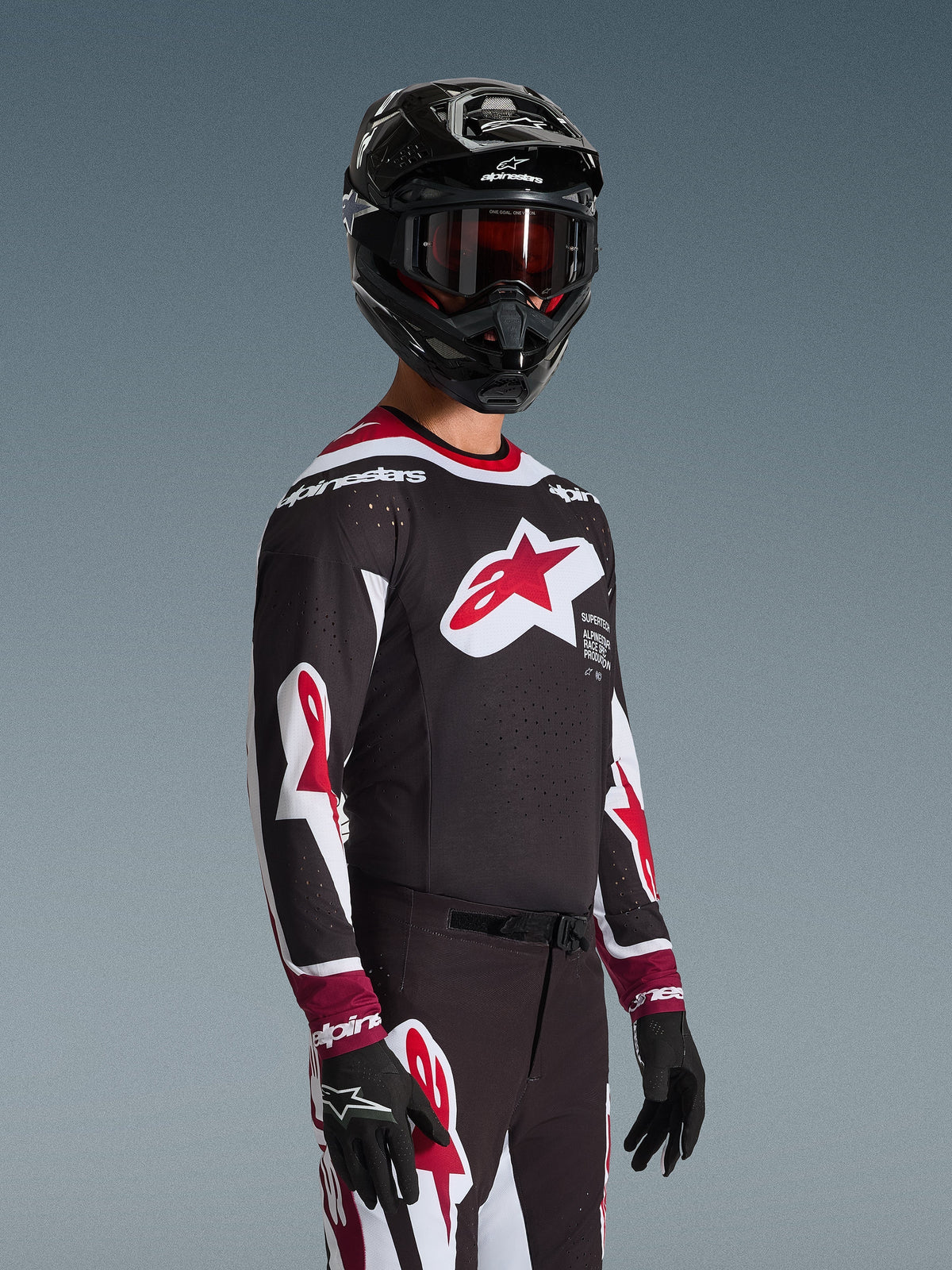 Piloto de motocross com a camisola Alpinestars 2026 Supertech AFD Vista em preto, vermelho e branco, com um grande logótipo de estrela vermelha no peito e perfurações cortadas a laser, combinada com um capacete preto e calças de corrida a condizer para desempenho off-road