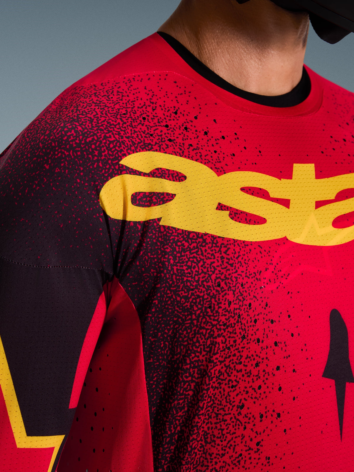 Grande plano da camisola Alpinestars Supertech Scenz 2026 em vermelho, preto e amarelo, apresentando um grande logótipo amarelo no peito, perfurações cortadas a laser para um fluxo de ar melhorado e uma textura de malha leve para motocross profissional.
