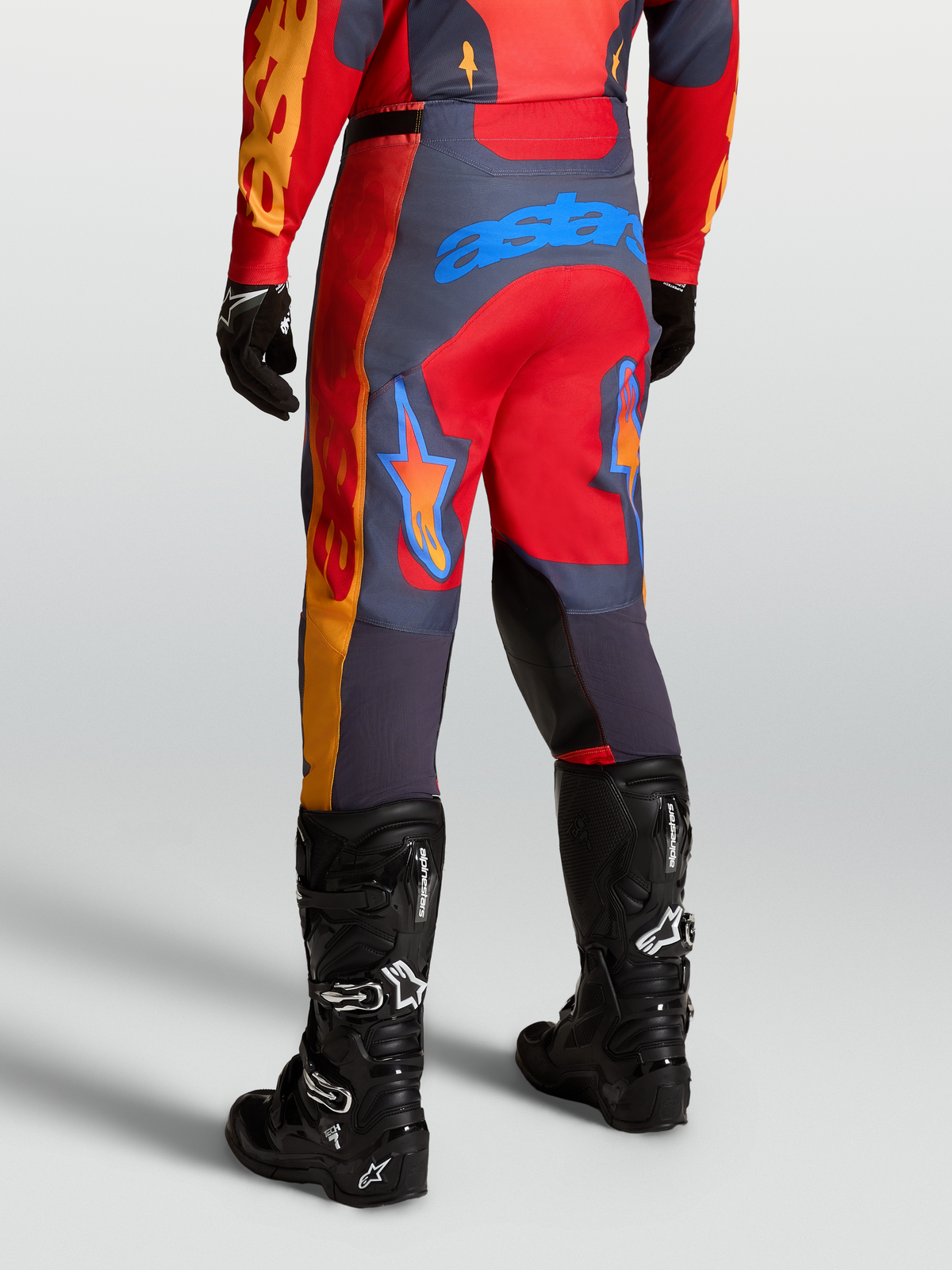 Alpinestars Calças Racer Hunt, calças de motocross para homem, vermelhas e cinzentas, vista traseira em posição de pilotagem off-road.