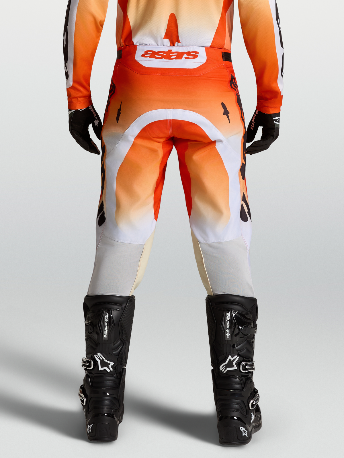 Alpinestars Calças Racer Amber, calças de motocross laranjas e brancas, ajuste de corrida, vista traseira no modelo com botas pretas