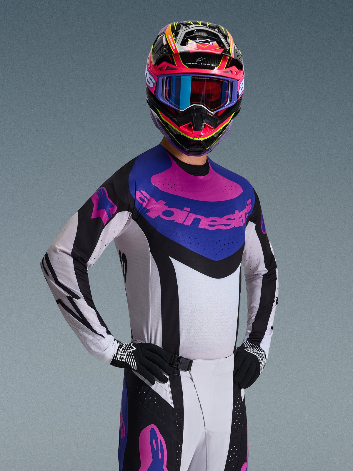 Camisola Techstar Knif 2026 da Alpinestars, camisola de motocross, preta, cinzento claro e roxa, usada por um piloto com equipamento completo, com estrutura branca, detalhes pretos e painel azul no peito com logótipo Alpinestars roxo, ajuste de alta performance para todo-o-terreno