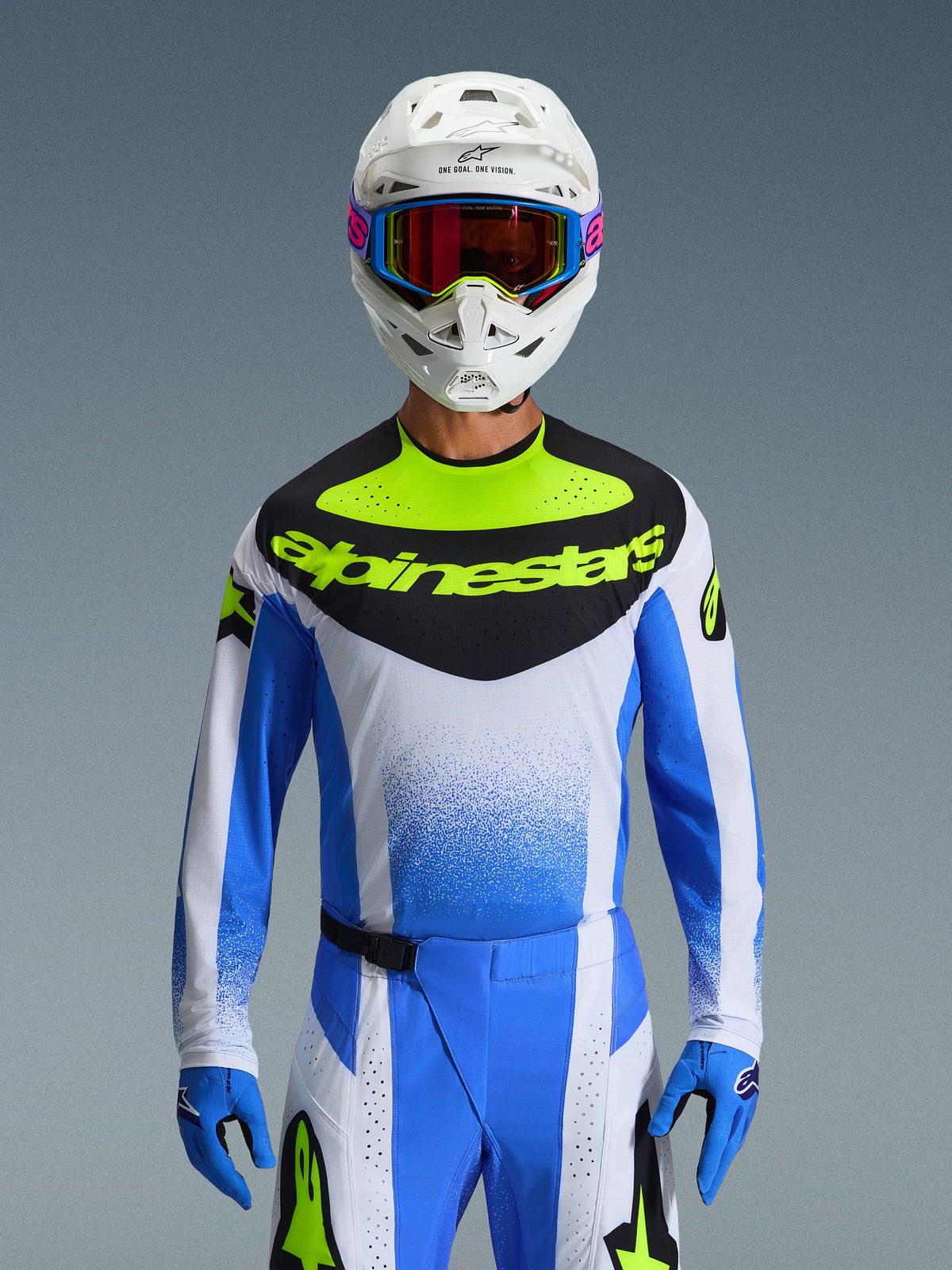Alpinestars 2026 Techstar Knif Gear Set, piloto de motocross com equipamento de corrida azul, branco e amarelo néon, camisola com painel frontal preto e logótipo amarelo néon, capacete branco com óculos coloridos, luvas e calças azuis a condizer, fato de corrida atlético de alta performance para competição todo-o-terreno