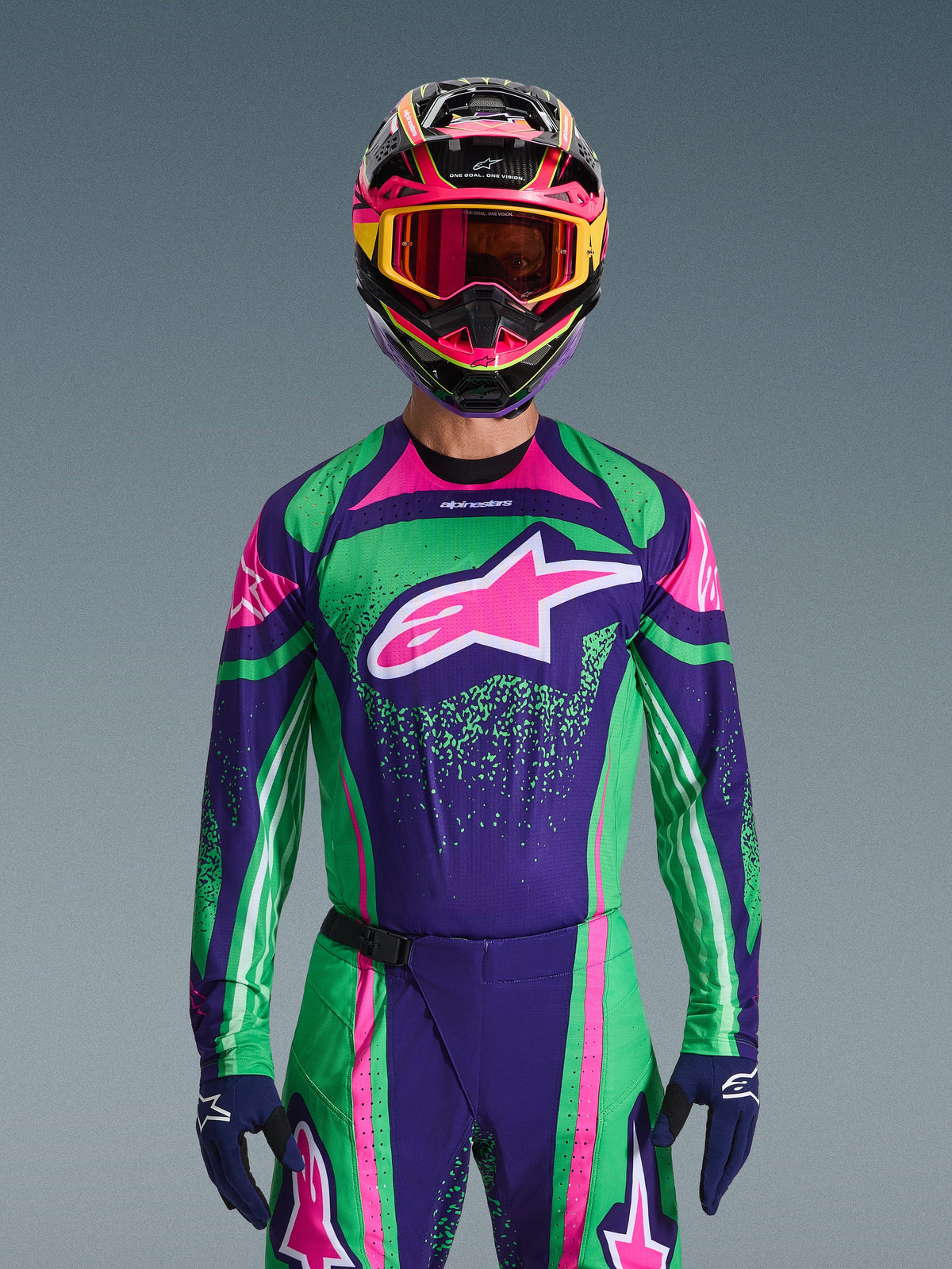 Conjunto de Equipamento Alpinestars 2026 Techstar Nomur, piloto de motocross a usar camisola de corrida em verde vibrante e roxo com detalhes cor-de-rosa, conjunto condizente com capacete e óculos multicoloridos, fato de motociclismo de alta performance para todo-o-terreno