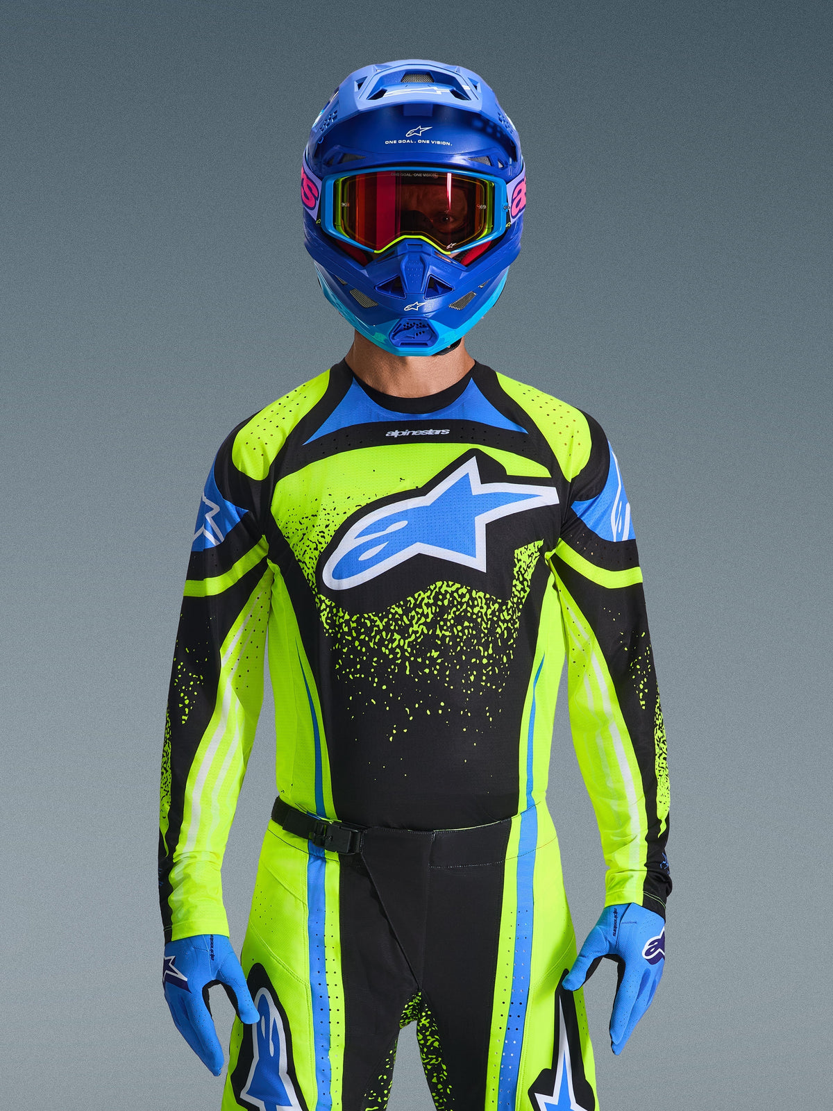 Piloto de motocross a usar a camisola Alpinestars 2026 Techstar Nomur em azul-escuro e amarelo néon com detalhes azuis, com um logótipo azul grande no peito, capacete e óculos azuis a condizer, equipamento de corrida coordenado para competição todo-o-terreno