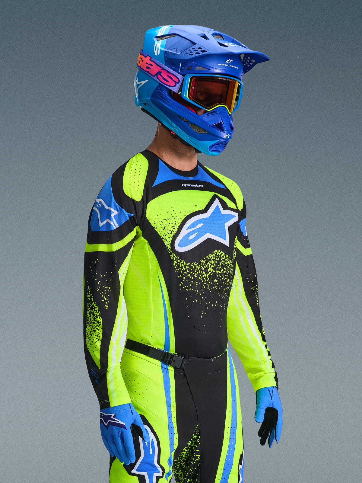 Piloto de motocross a usar a Camisola Techstar Nomur 2026 em azul marinho e amarelo néon, combinada com calças a condizer, um capacete de corrida azul e óculos, apresentando um logótipo Alpinestars grande e corte atlético de corrida para desempenho todo-o-terreno.
