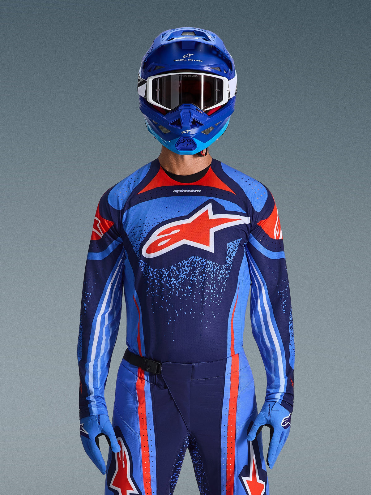 Piloto de motocross a usar a camisola Alpinestars 2026 Techstar Nomur em azul-marinho, laranja e azul UCLA, calças a condizer e luvas azuis, capacete azul com óculos brancos, logótipo Alpinestars grande em vermelho e branco no peito, equipamento de performance coordenado para corridas off-road.