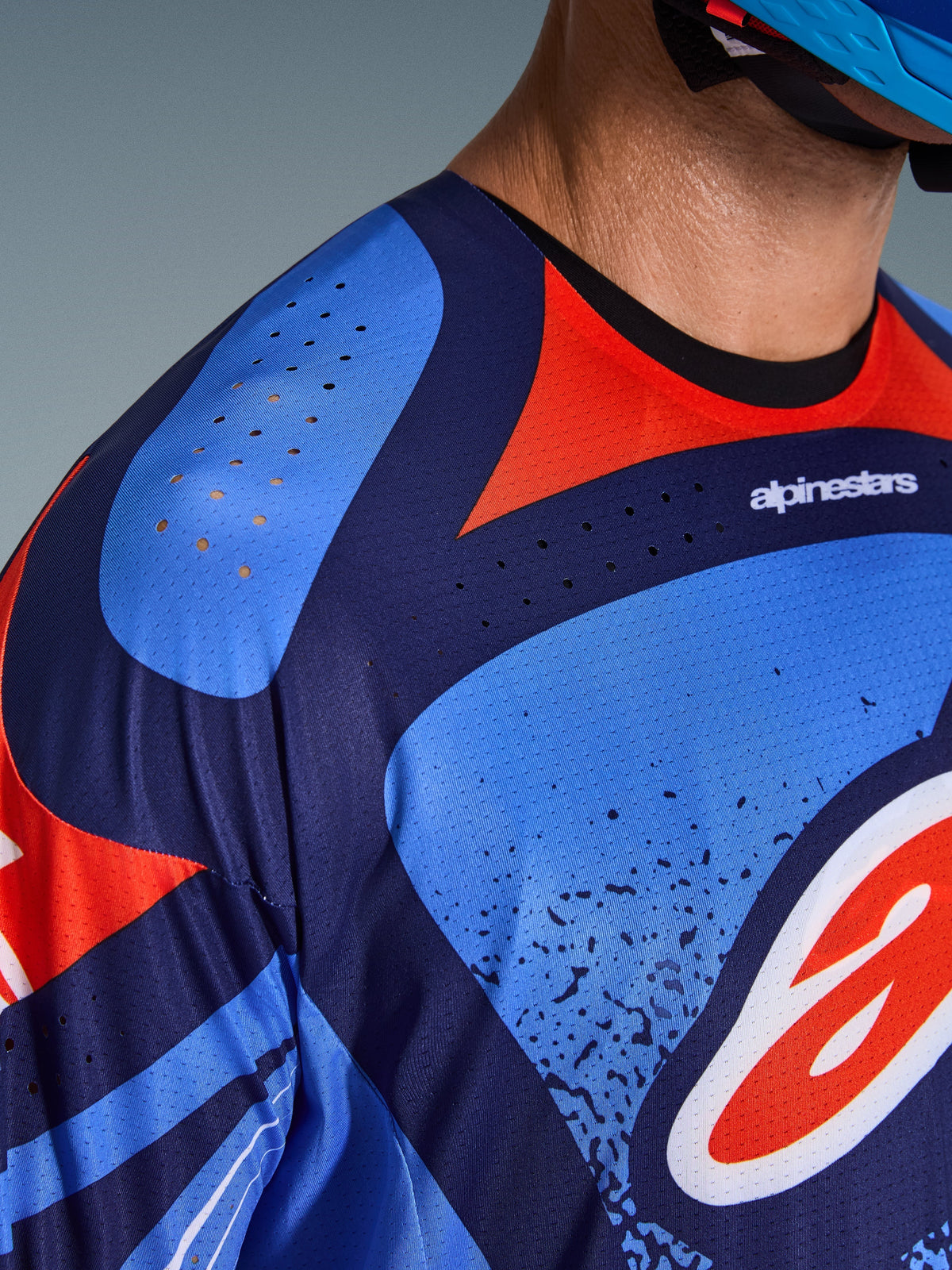Grande plano da camisola Alpinestars 2026 Techstar Nomur, camisola de motocross, azul marinho escuro, laranja e azul UCLA, com perfurações de ventilação a laser no ombro e no peito, tecido técnico de absorção de humidade e design de ajuste atlético de corrida