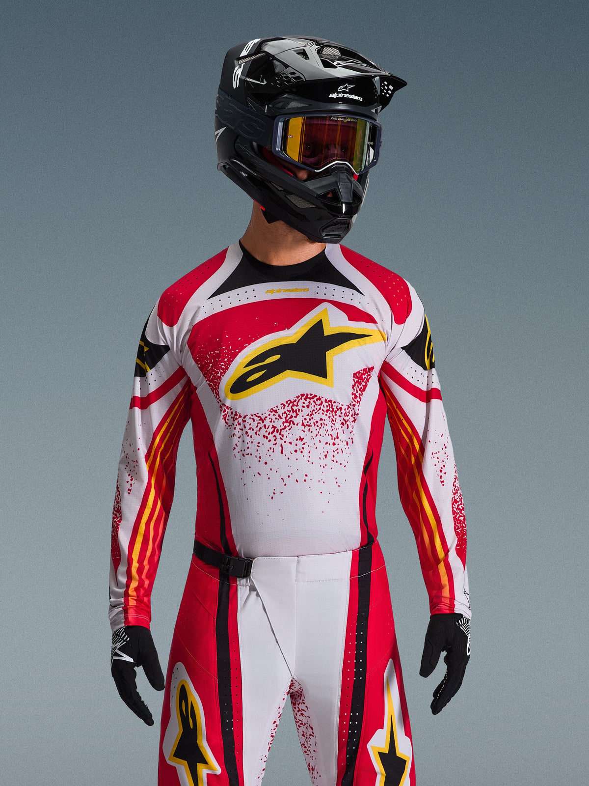 Conjunto de Equipamento Alpinestars Techstar Nomur 2026, piloto de motocross a usar camisola vermelha, branca e preta com logótipo amarelo, calças a condizer com padrão salpicado, capacete e óculos de proteção pretos, luvas pretas, equipamento de corrida completo para competição todo-o-terreno