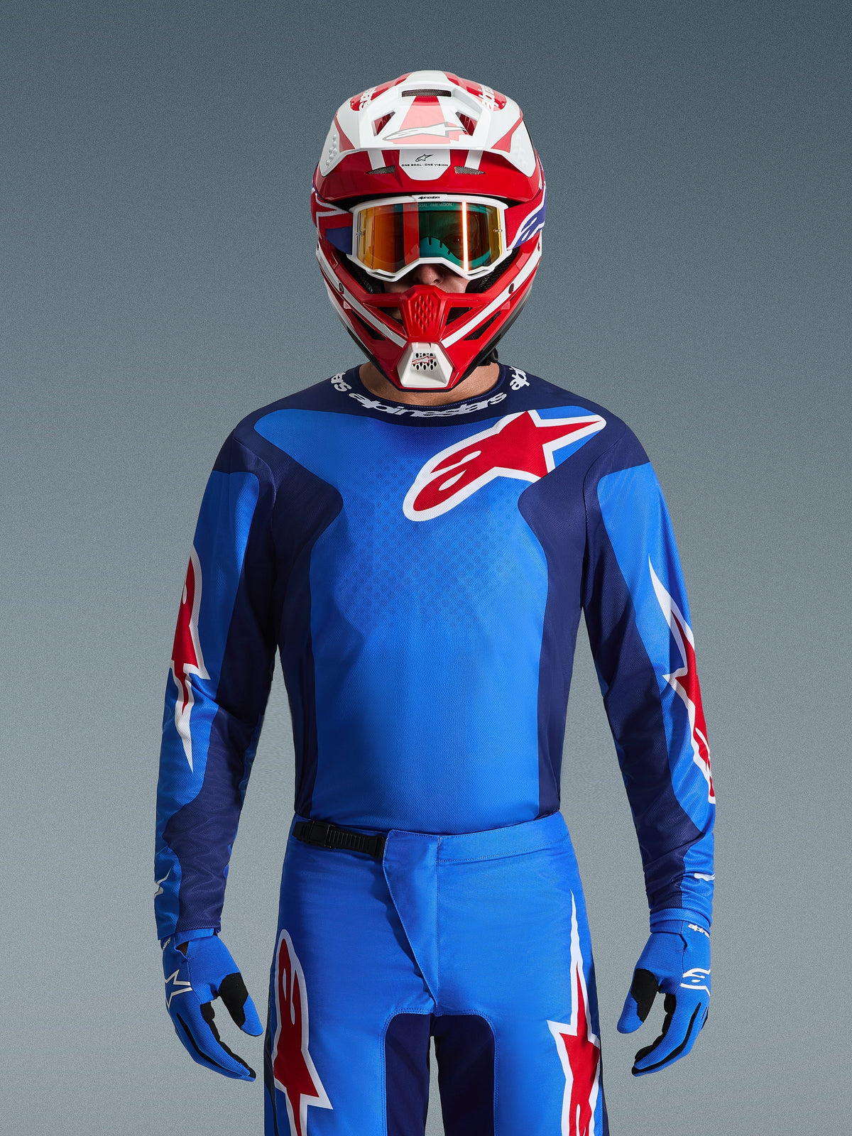 Alpinestars 2026 Fluid Grid Jersey, camisola de motocross azul e vermelha, usada com calças a condizer e um capacete vermelho e branco, com logótipos de estrela vermelha proeminentes e um ajuste atlético concebido para performance em corridas todo-o-terreno