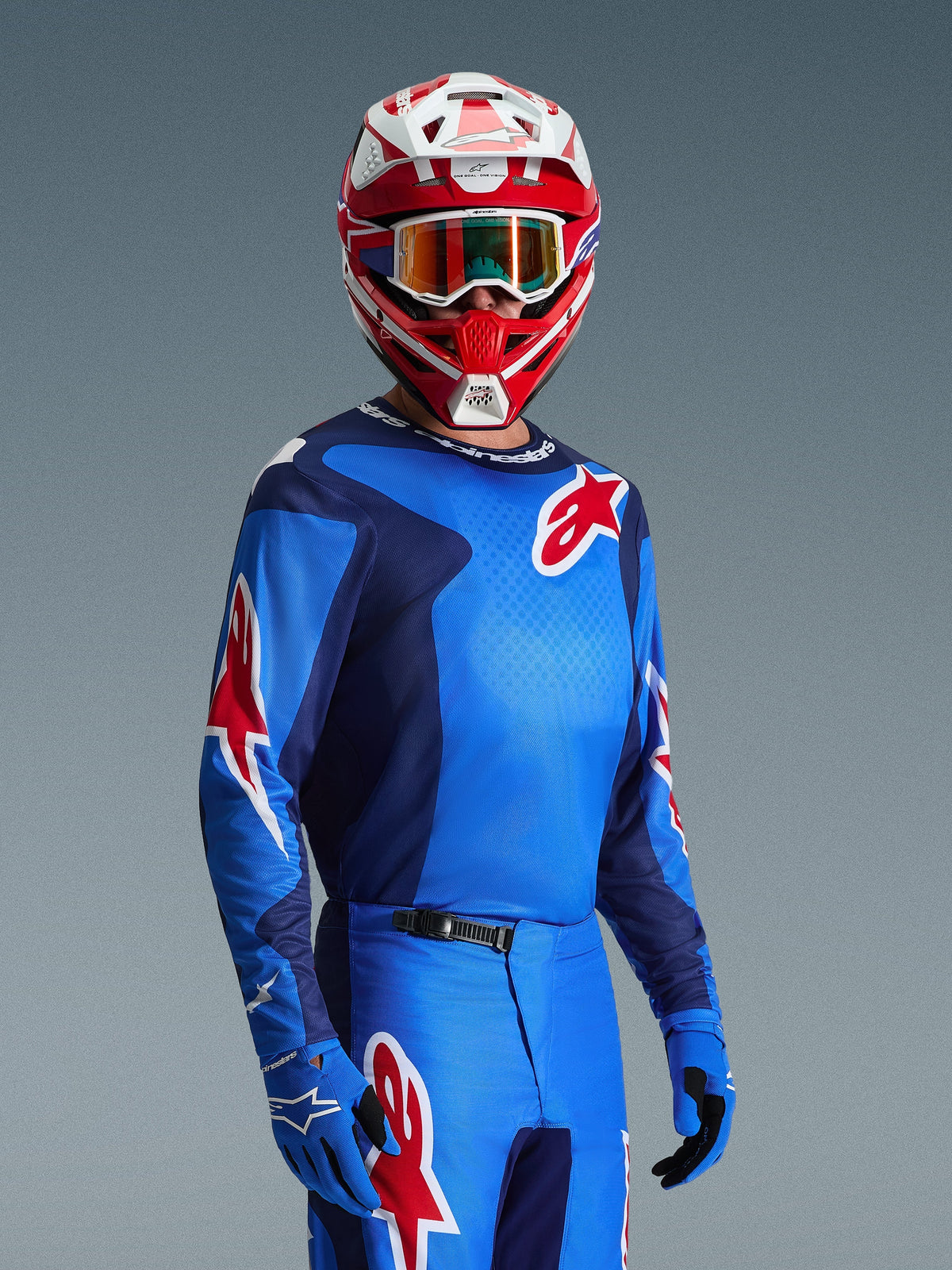 Piloto de motocross a usar a Camisola Alpinestars Fluid Grid 2026 em azul e vermelho, com logótipos de estrela vermelhos da Alpinestars, combinada com calças azuis a condizer, luvas azuis e um capacete vermelho e branco com óculos de proteção