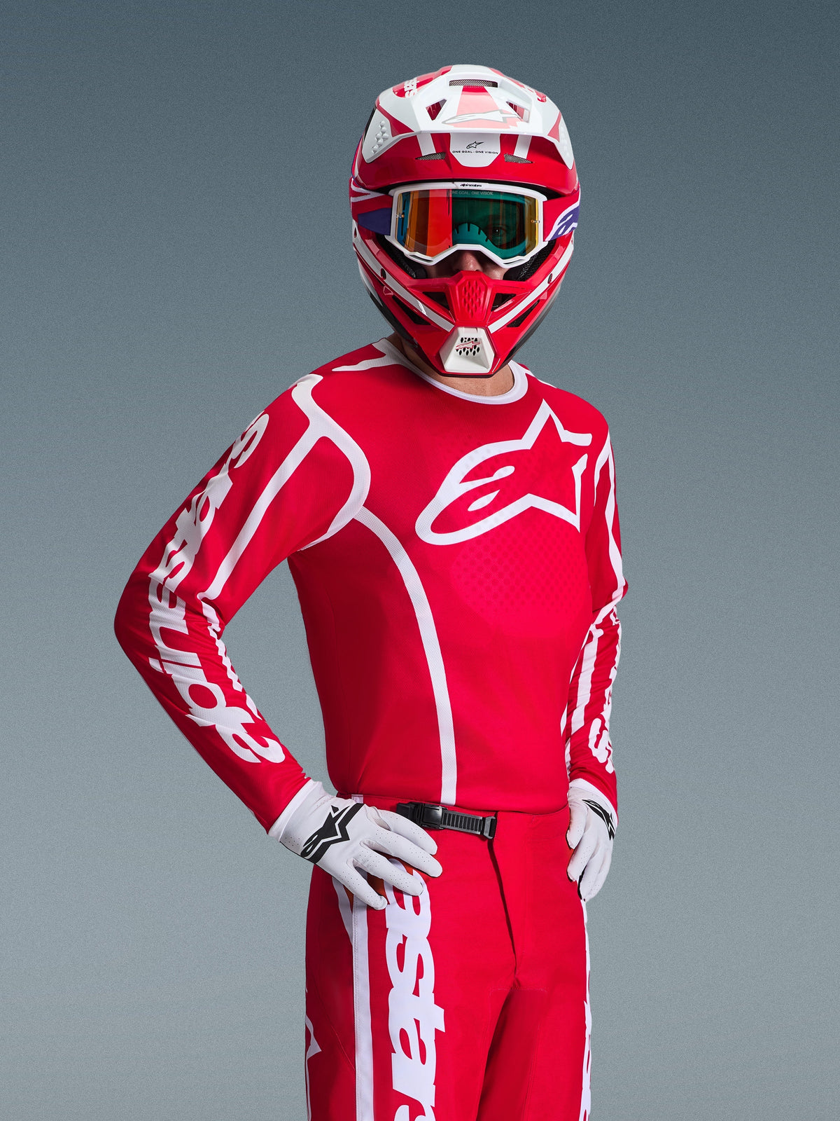 Piloto de motocross a usar a Camisola Alpinestars Fluid Apex 2026 em vermelho e branco, capacete vermelho e branco a condizer com óculos, luvas brancas e calças vermelhas, com logótipos brancos proeminentes e ajuste atlético, num conjunto coordenado para corridas de off-road
