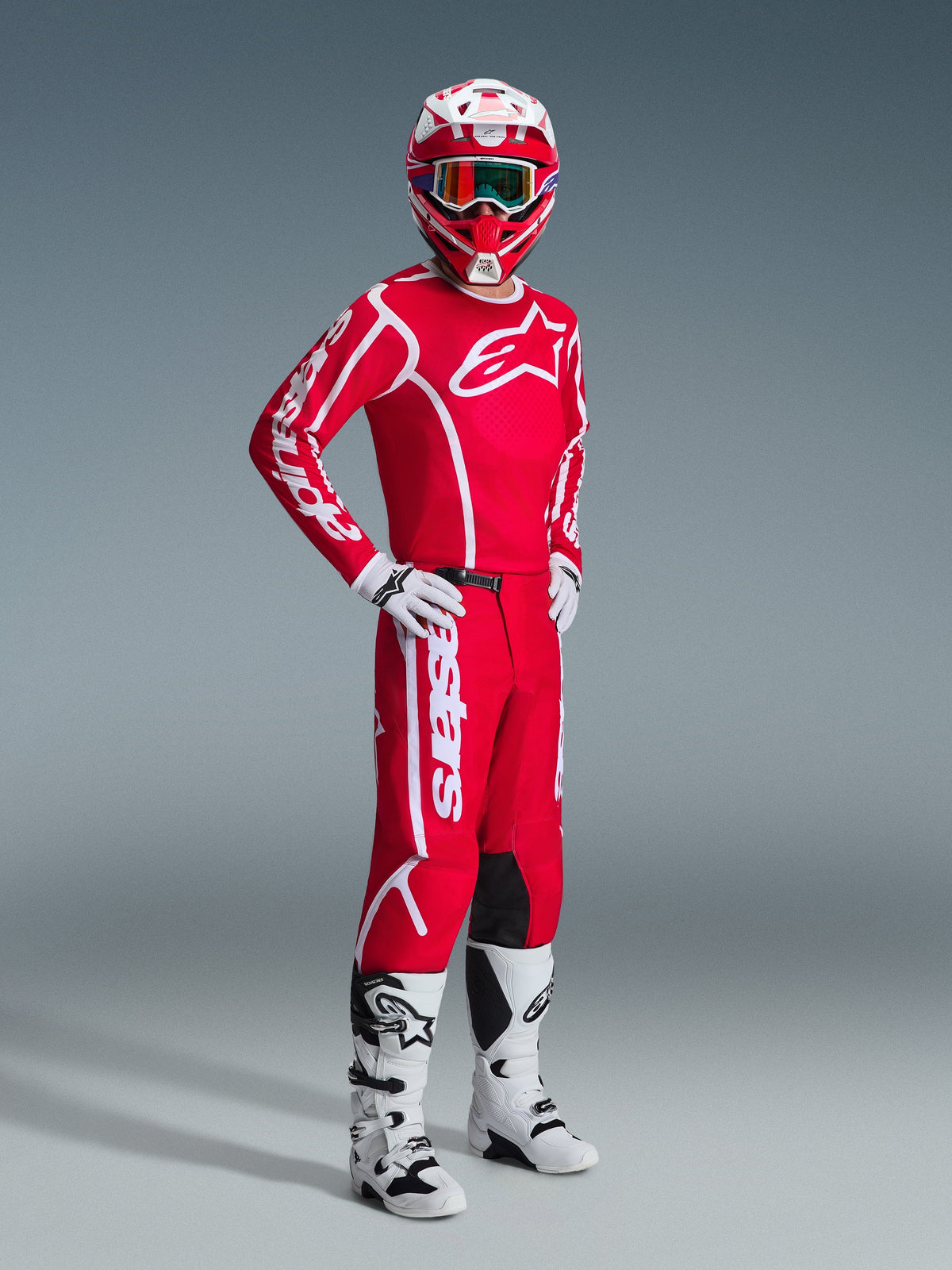 Piloto de motocross com equipamento Alpinestars completo, apresentando a Camisola Fluid Apex 2026 em Vermelho e Branco, calças vermelhas a condizer com logótipo branco, capacete vermelho e branco com óculos, botas de motocross brancas e pretas e luvas brancas, fotografia profissional de estúdio de equipamento off-road.