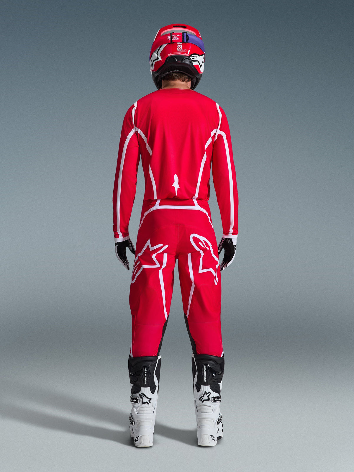 Piloto de motocross visto de trás a usar a camisola Alpinestars 2026 Fluid Apex em vermelho e branco, calças vermelhas a condizer com logótipos de estrela brancos proeminentes, capacete vermelho, botas de motocross brancas e pretas e luvas pretas e brancas, kit completo para corridas off-road
