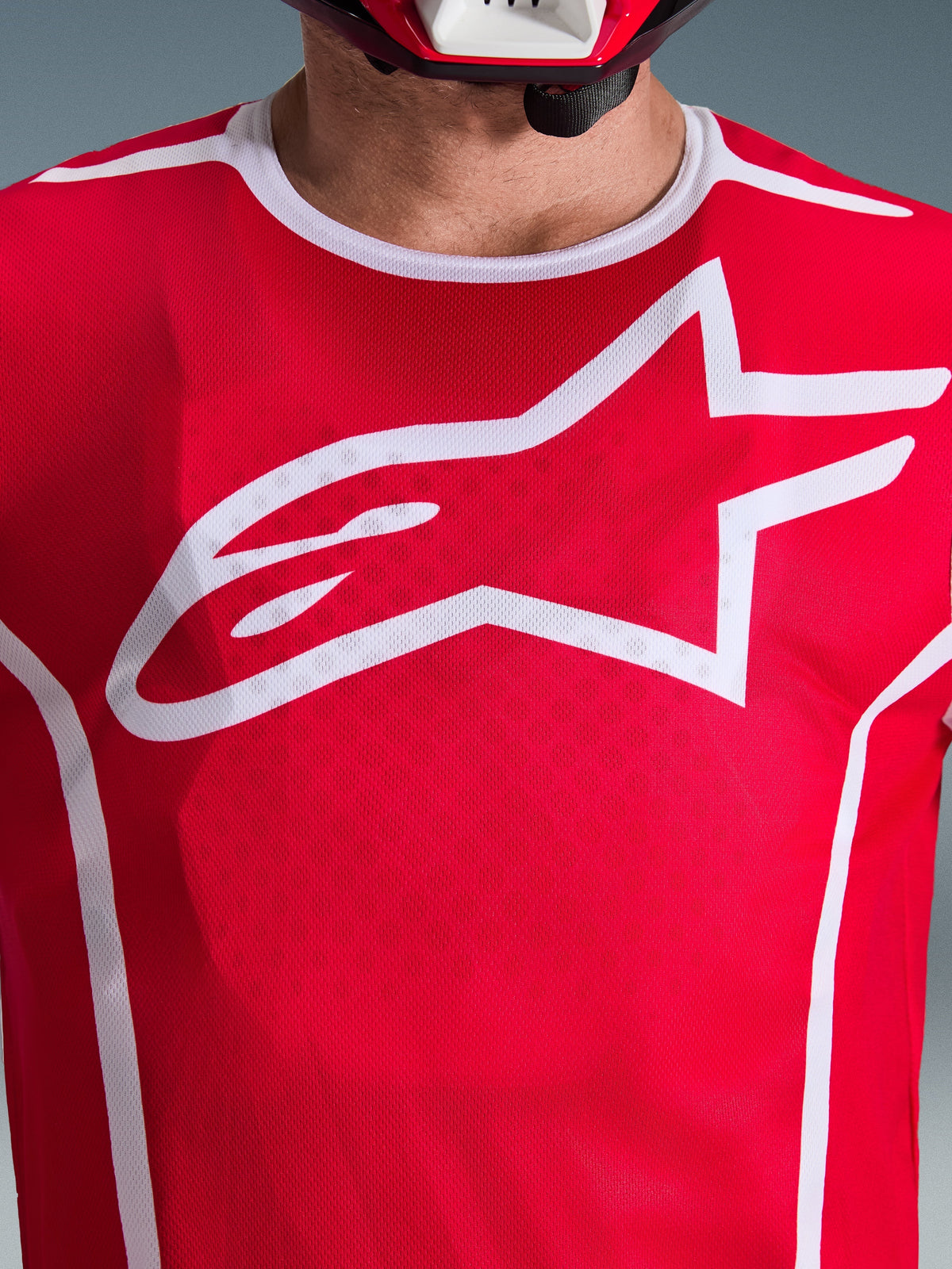 Camisola Alpinestars 2026 Fluid Apex, vermelha e branca, vista de perto do peito com grande logótipo Astars branco, gola desportiva branca e tecido que absorve a humidade para desempenho em motocross