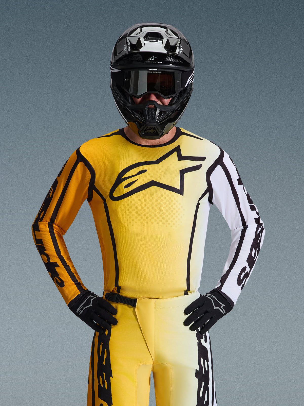 Piloto de motocross a usar o Alpinestars 2026 Fluid Apex Gear Set, camisola amarela e branca com grande logótipo de estrela preto, calças amarelas e brancas a condizer, capacete preto com óculos de proteção pretos e luvas pretas, conjunto coordenado para corridas fora de estrada
