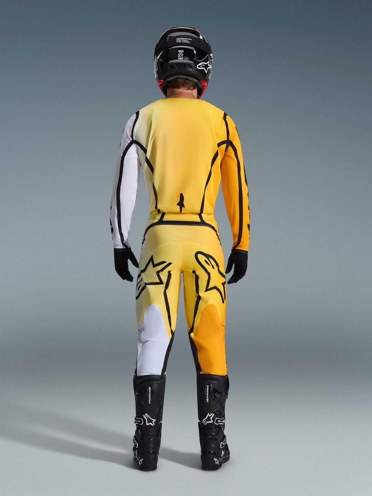 Motocross rider from behind wearing Alpinestars 2026 Fluid Apex Jersey and matching pants in Yellow Black, featuring bold color-blocked panels in white, yellow, and orange, paired with a black helmet and motocross boots.