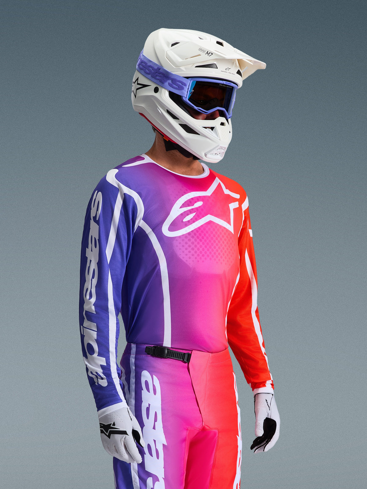 Alpinestars 2026 Fluid Apex Jersey, Motocross Jersey, vibrant purple pink and orange gradient, worn with matching pants, white helmet with blue goggles, and white gloves, athletic design for off-road performance and mobility