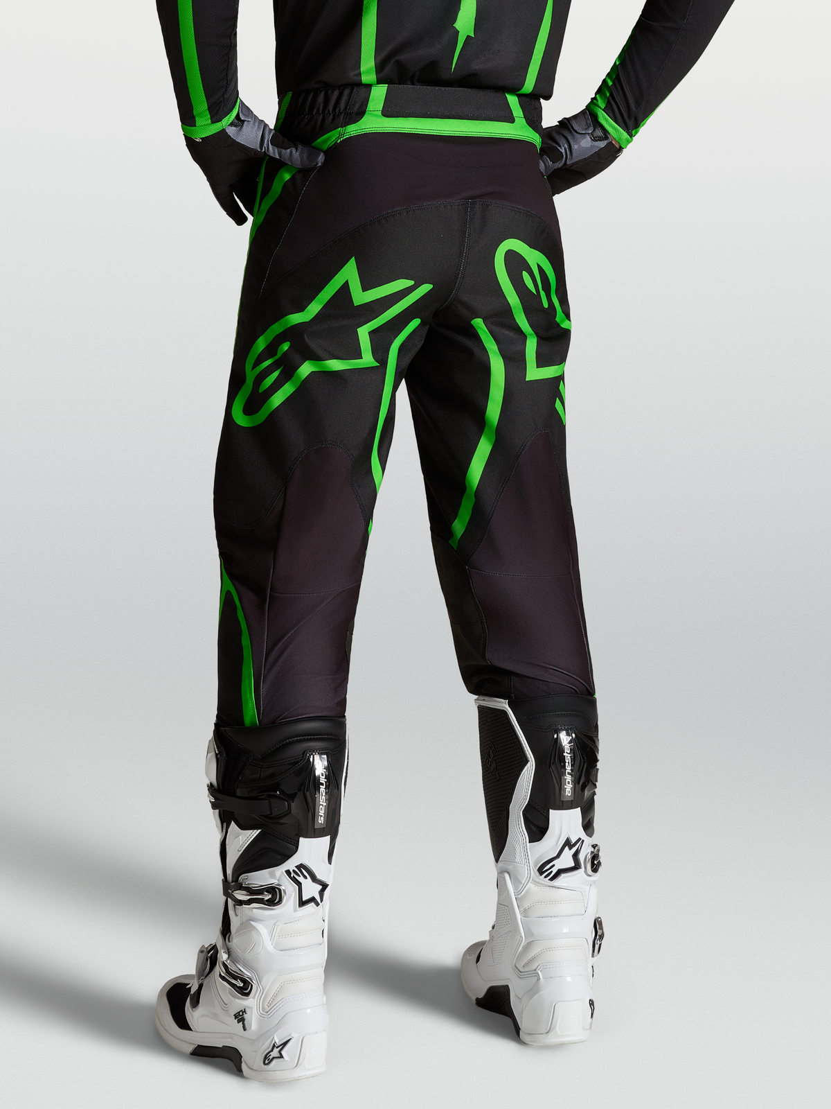 Alpinestars Fluid Apex V2, calças de motocross para homem, pretas e verdes fluo, vista traseira no modelo com botas brancas.