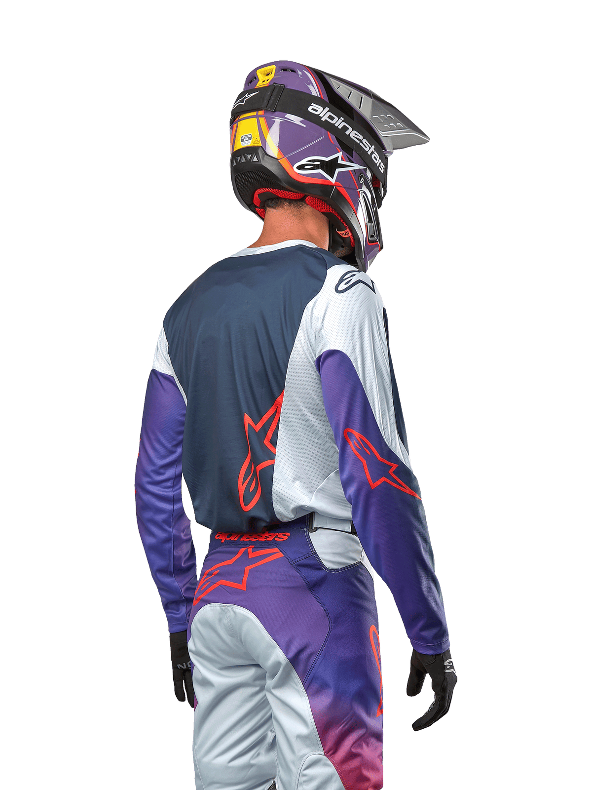 Piloto de motocross visto de costas a usar a camisola Alpinestars 2024 Racer Hoen, painel traseiro azul-marinho com ombros cinza-claro e mangas roxas, logótipos Alpinestars em cor de laranja vibrante, calças roxas e cinzentas a condizer com capacete de motocross roxo, kit completo de competição todo-o-terreno
