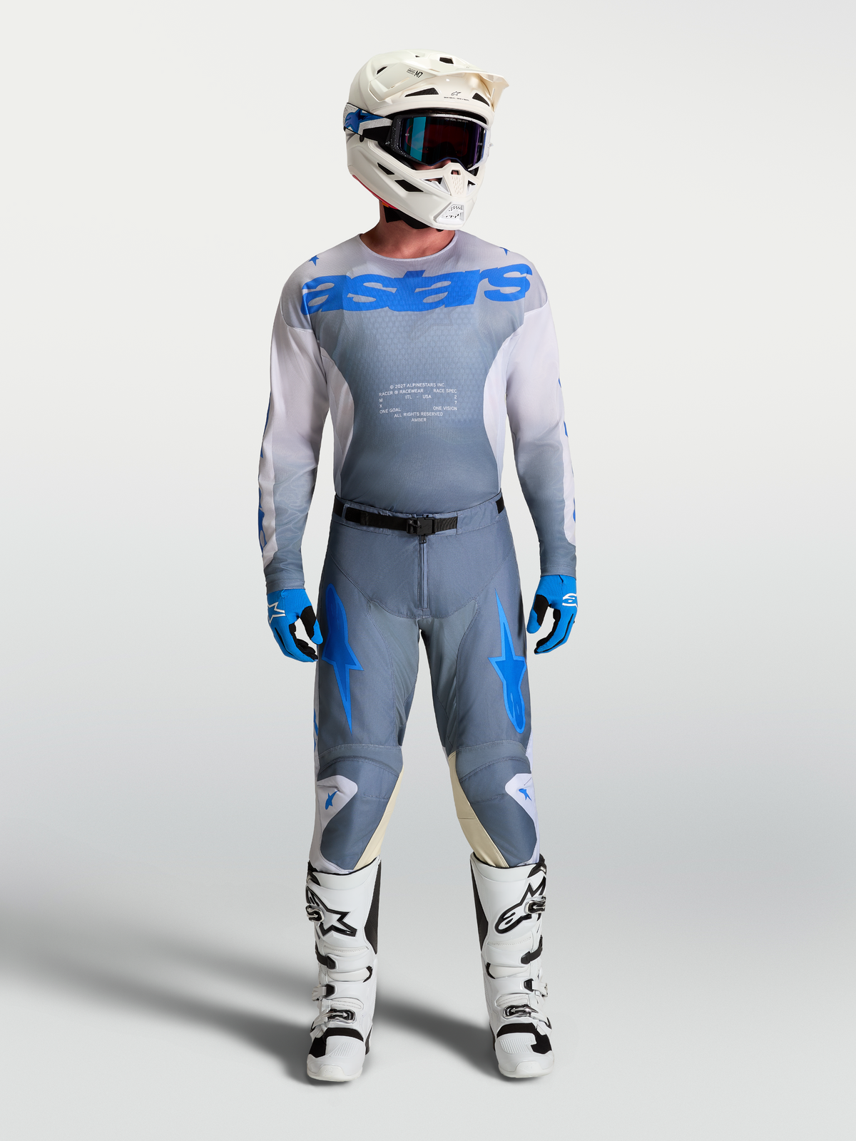 Alpinestars Racer Amber, calças e camisola de motocross para homem, cinzento e azul, com botas e capacete brancos.