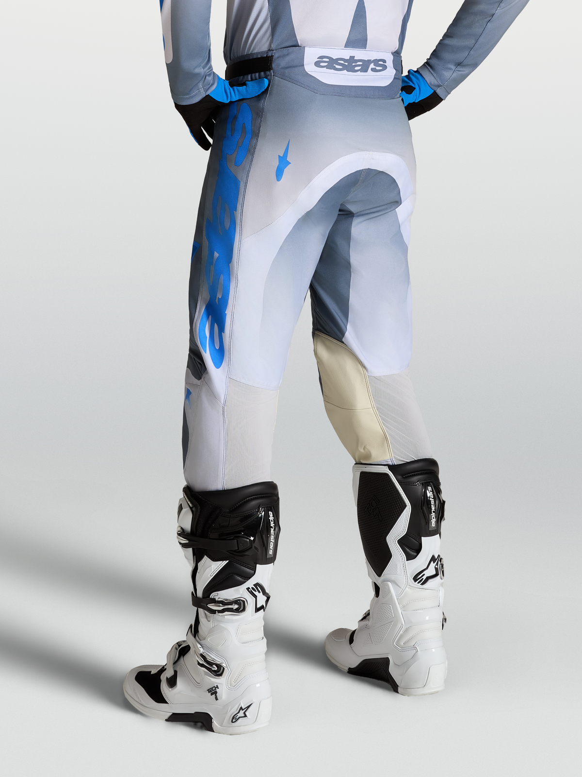 Alpinestars Calças Racer Amber, calças de motocross para homem, cinzento, azul e branco, vista traseira, painéis de pele nos joelhos e ventilação traseira