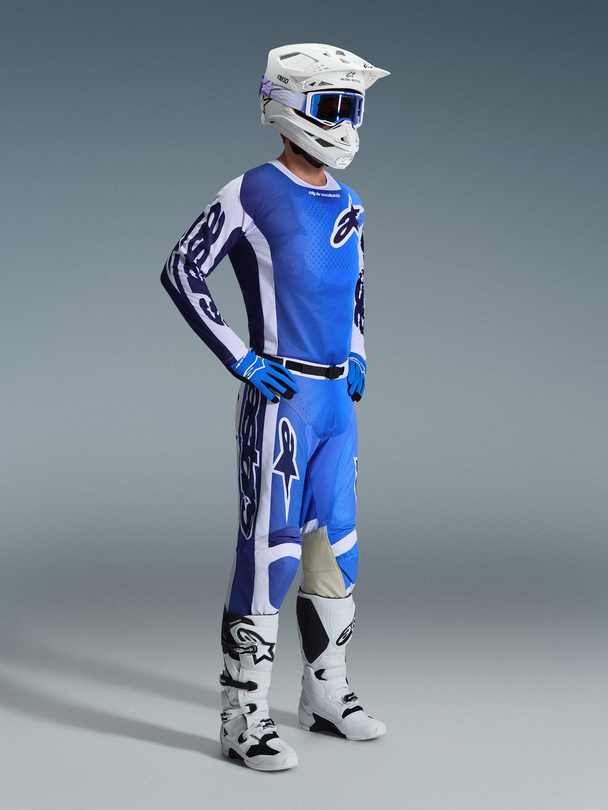 Piloto de motocross a usar a Camisola Alpinestars 2026 Racer Air Portl em Azul Ucla e Branco, combinada com calças azuis e brancas a condizer, capacete branco, óculos azuis e botas brancas e pretas, kit completo de corrida off-road