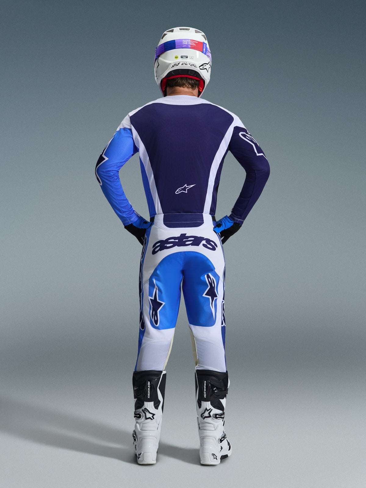 Vista traseira de um piloto de motocross com a Camisola Alpinestars 2026 Racer Air Portl em Ucla Blue White, combinada com calças brancas e azuis a condizer e botas brancas, destacando a construção em malha de fluxo de ar total nas costas para corridas off-road.