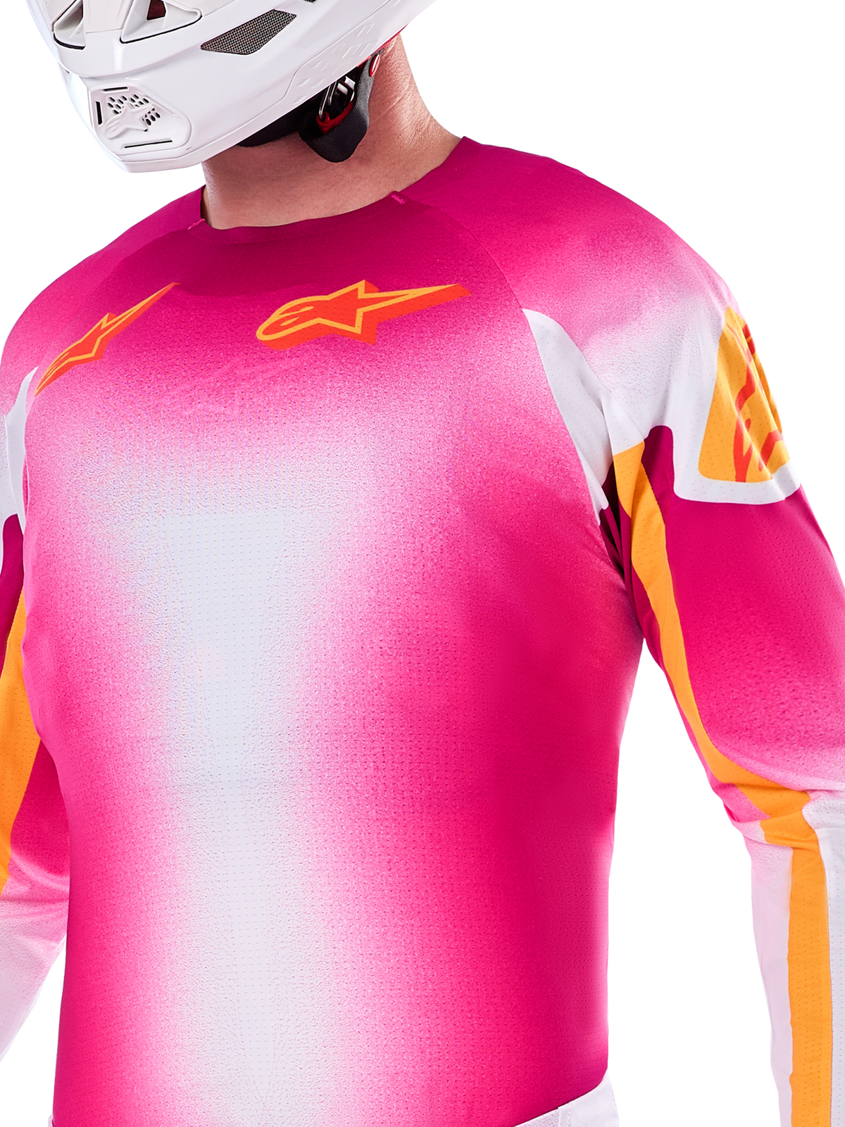 Alpinestars Limited Edition Supertech AFD MIG Jersey, camisola de motocross em gradiente de rosa néon e branco, com logótipos Astars cor de laranja e detalhes nas mangas, usada por um piloto com capacete branco, corte atlético de competição