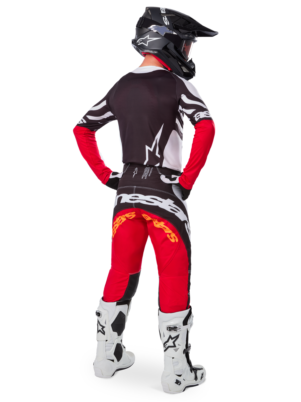 Vista traseira de um piloto de motocross a usar o conjunto de equipamento Limited Edition Techstar Deep, com camisola preta com detalhes brancos e vermelhos, calças vermelhas e pretas a combinar com a marca 'Alpinestars', botas de corrida brancas e capacete preto, exibindo o equipamento completo de corrida off-road.