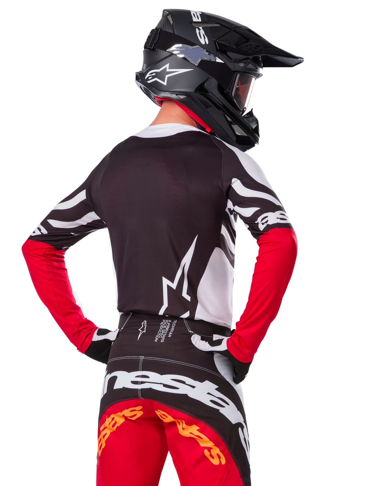 Piloto de motocross com equipamento de corrida completo, Camisola Alpinestars Techstar Deep Edição Limitada em preto, branco e vermelho High Red, vista de costas, calças Techstar Deep a condizer, capacete preto com óculos, luvas pretas e brancas, equipamento profissional de corrida todo-o-terreno