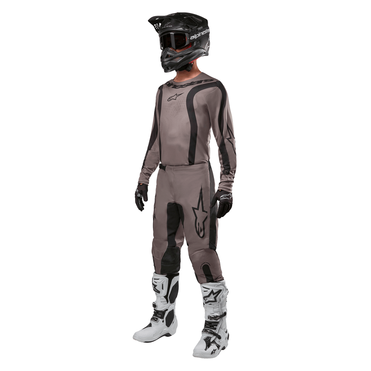 Piloto de motocross a usar equipamento de corrida completo com a camisola Alpinestars 2024 Fluid Lurv em Mud Black, combinada com calças a condizer, capacete preto com óculos, botas brancas e pretas e luvas pretas, conjunto coordenado para corridas todo-o-terreno