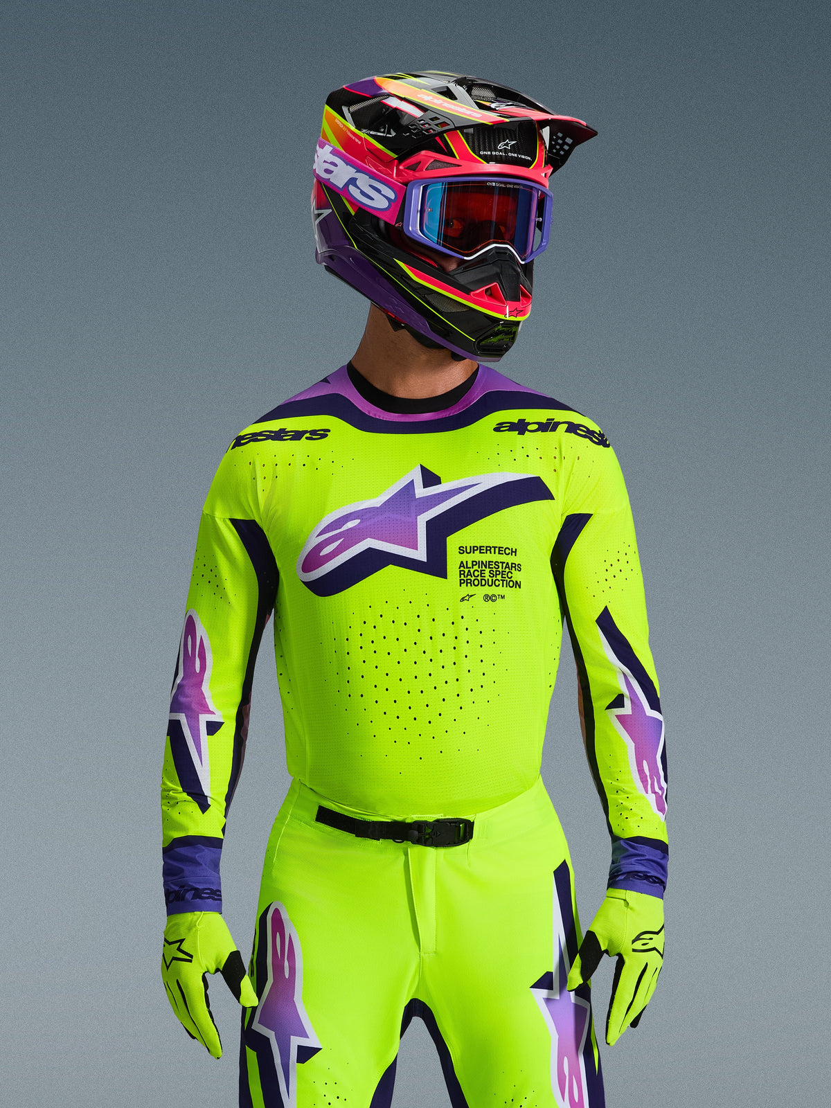 Alpinestars 2026 Supertech Vista Gear Set, motocross rider wearing high-visibility yellow jersey and pants with purple and blue accents, large Alpinestars logo on chest, matching colorful helmet and goggles, pro-level racing outfit