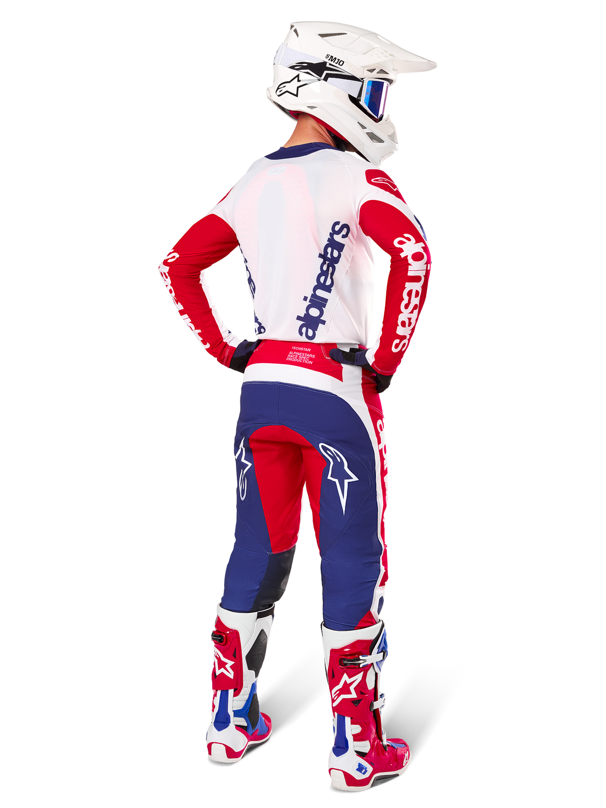 Piloto de motocross visto de costas a usar a camisola e o conjunto de equipamento Techstar Fortitude Edição Limitada da Alpinestars, nas cores vermelho brilhante, branco e azul, com a marca Alpinestars em branco nas mangas vermelhas e logótipo azul-marinho nas costas brancas, combinado com um capacete de motocross branco e botas de competição a condizer.