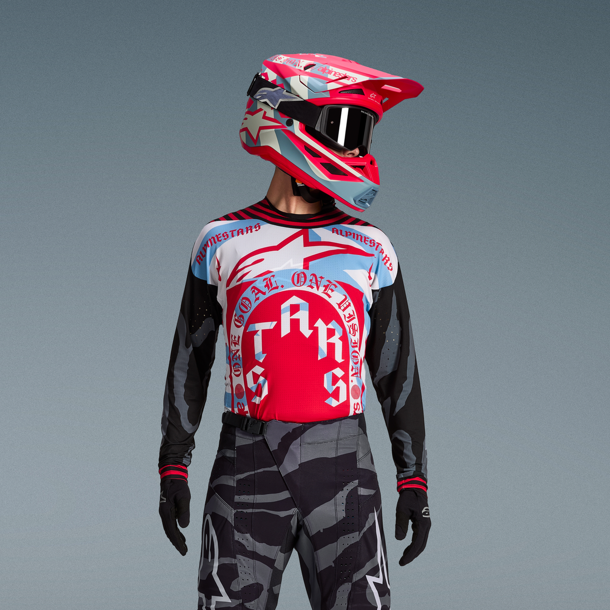 Conjunto Techstar Beast Coast, camisola vermelha e azul com calças camufladas e capacete de motocross em cores vibrantes.