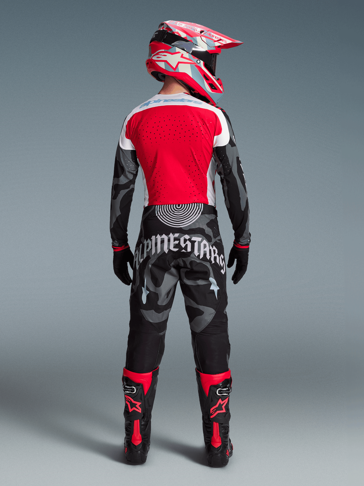 Conjunto Alpinestars Techstar Beast Coast Edição Limitada, piloto de costas com camisola vermelha e calças de camuflagem pretas.