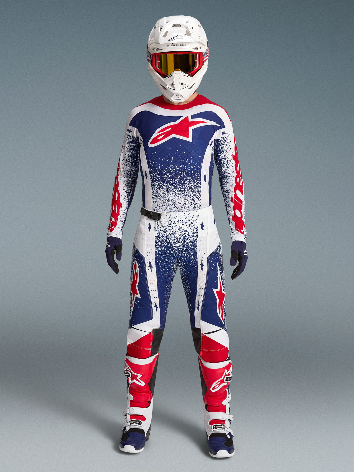 Alpinestars Techstar Unity Jersey Edição Limitada, camisola de motocross para homem, azul, branca e vermelha com gráficos salpicados, vista frontal em conjunto de equipamento de todo-o-terreno.
