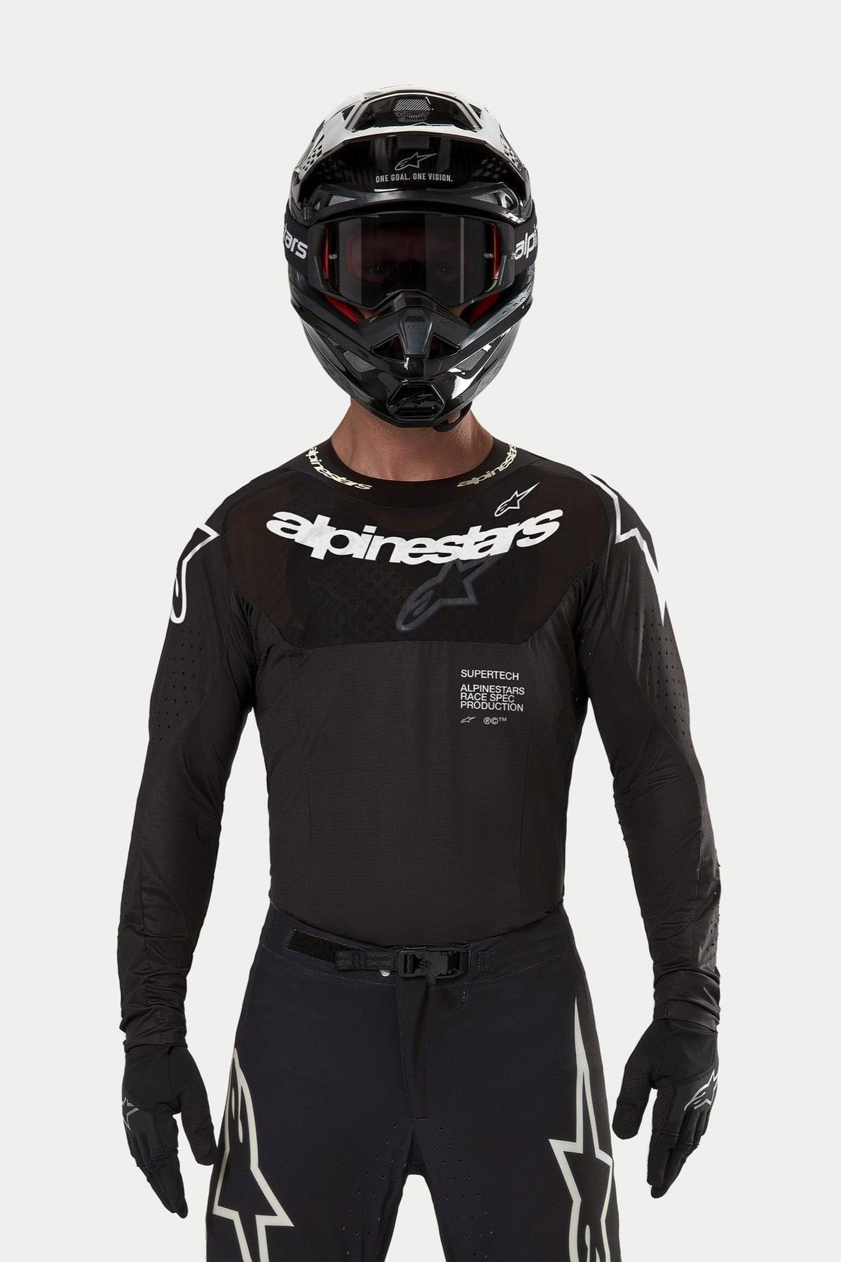 Piloto de motocross a usar a camisola Alpinestars Supertech Ward 2024 em preto, corte atlético de corrida com logótipo Alpinestars branco no peito, apresentando perfurações cortadas a laser e o texto 'Supertech Race Spec', combinada com um capacete preto e óculos para corridas todo-o-terreno.