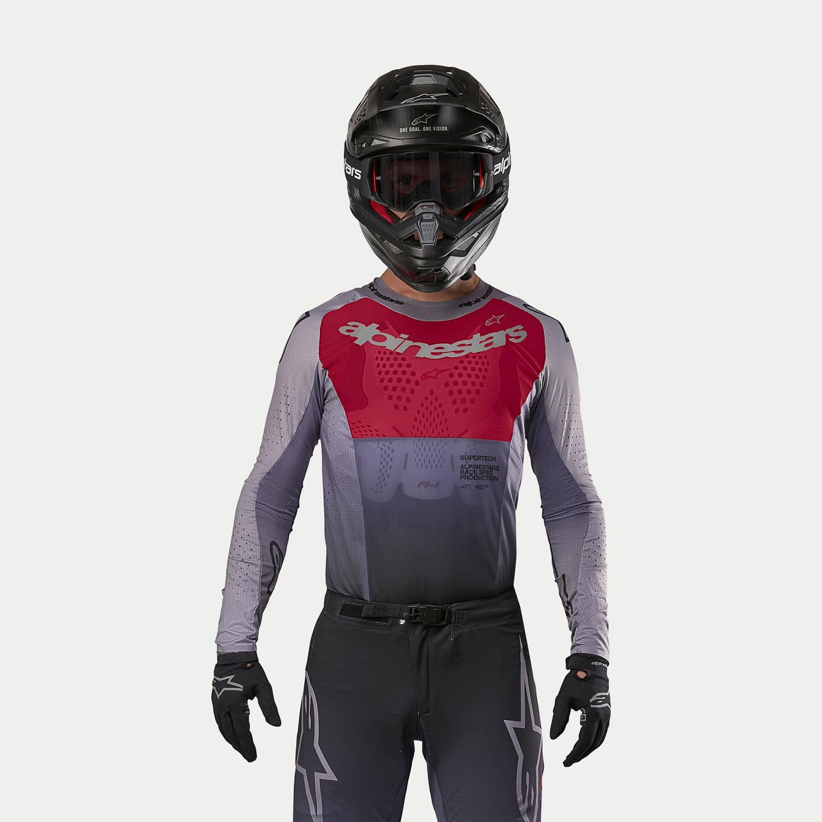 Piloto de motocross a usar a camisola Alpinestars 2024 Supertech Dade em Iron Red Berry, com um painel vermelho no peito e mangas cinzentas com logótipo prateado, usada com calças a condizer, capacete preto e luvas pretas, equipamento profissional de corrida off-road