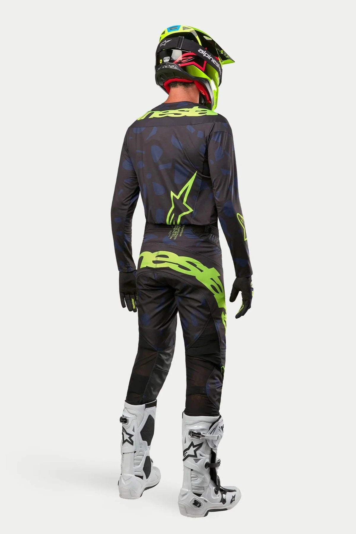 Camisola e Calças Alpinestars 2024 Techstar Rantera, piloto de motocross com equipamento completo visto de trás, em preto, azul marinho e amarelo fluo, capacete amarelo fluo a condizer e botas brancas, kit de corrida todo-o-terreno coordenado