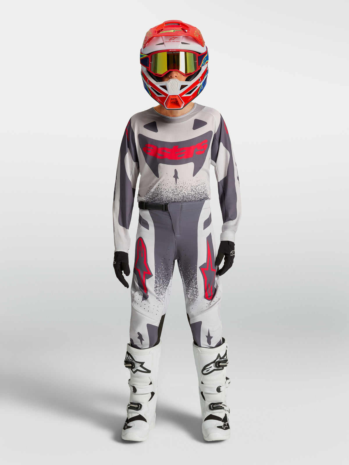 Alpinestars Supertech Swan 2027 para jovens, conjunto de motocross cinzento e branco com pormenores vermelhos.