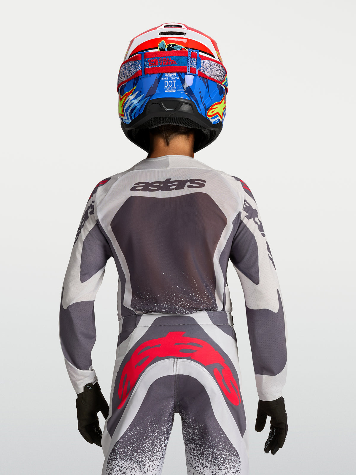 Alpinestars Juventude Supertech Swan, camisola e calças de motocross, cinzento e branco com pormenores vermelho fluo, vista traseira no piloto.